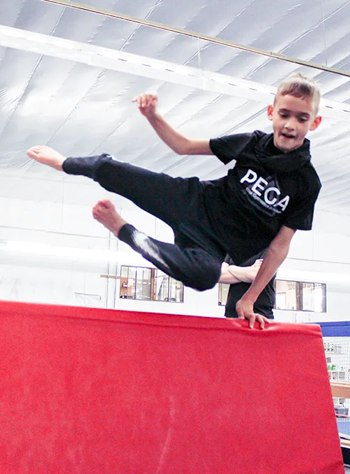 A boy in a PEGA shirt mid-vault in the parkour class